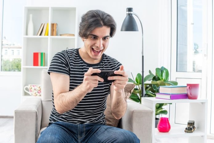 young-man-casual-clothes-playing-games-using-smartphone-happy-excited-sitting-chair-light-living-room_141793-98670